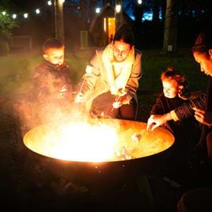 A family toasting marshmallows by the firepit at Pinewood glamping pods at Port Lympne Hotel & Reserve in Kent, UK