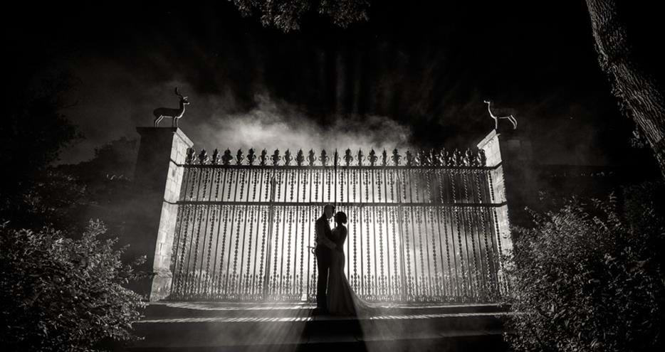 Newly married couple, backlit in the dark and fog by the gates to the historic gardens at Port Lympne Hotel & Reserve, Kent wedding venue